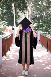 Full length of woman holding mortarboard on street