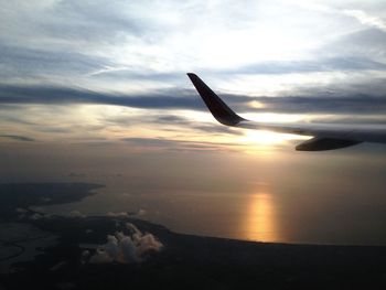 Airplane flying over sea against sky during sunset