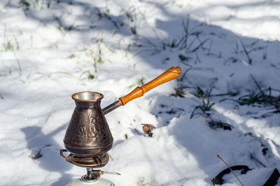 Copper turk with a wooden handle for making coffee on a background of snow in woods