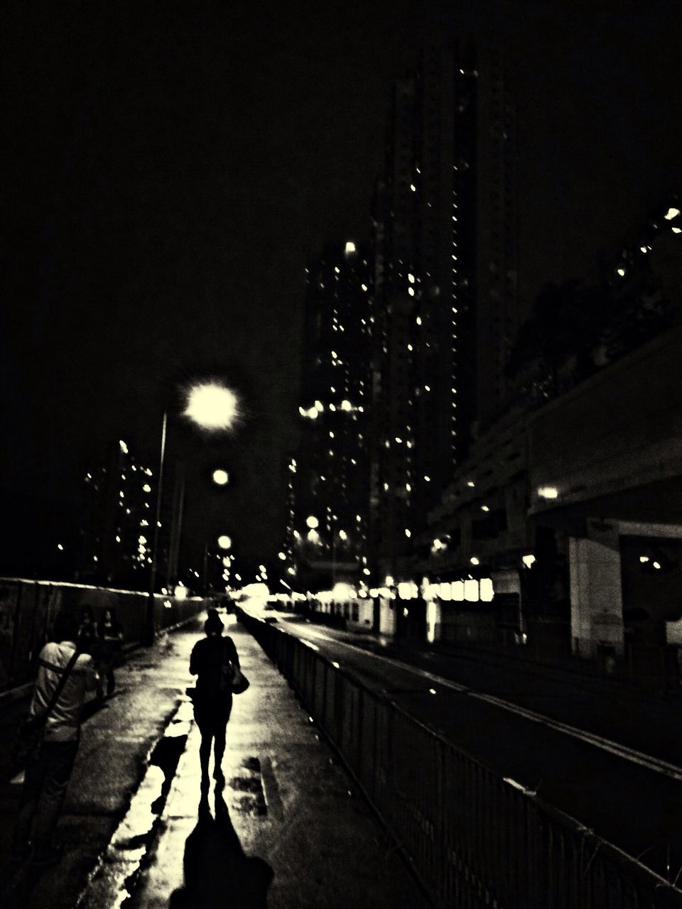 night, illuminated, city, building exterior, street, architecture, built structure, street light, walking, city life, lifestyles, full length, men, road, transportation, rear view, city street, the way forward