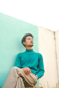 Low angle view of young man looking away against wall