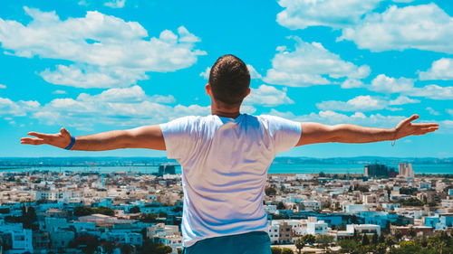 Rear view of man standing by cityscape against sky