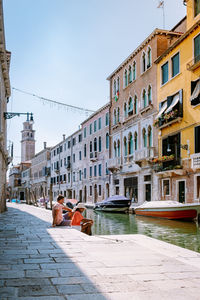 People on building by canal against sky in city