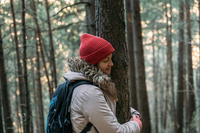 Side view of woman wearing hat against trees in forest during winter