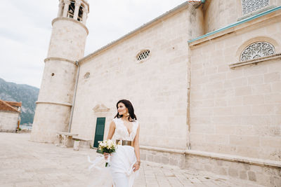 Woman with umbrella standing against built structure