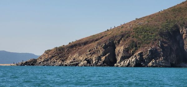 Scenic view of sea by mountain against clear blue sky