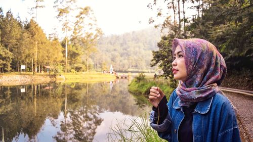 Portrait of woman looking at lake against trees