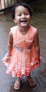 Portrait of cheerful baby girl standing on wet footpath