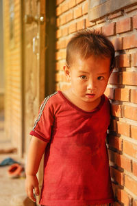 Portrait of cute baby boy standing by brick wall