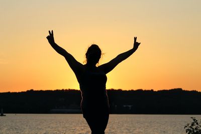 Silhouette woman standing at beach against sky during sunset