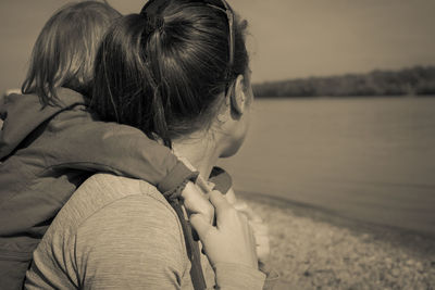 Side view of woman giving piggy back ride to daughter at riverbank