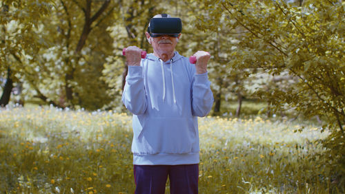 Senior man wearing vr goggles and exercising with dumbbells in park