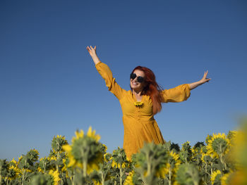 Low angle view of woman with arms raised standing against blue sky