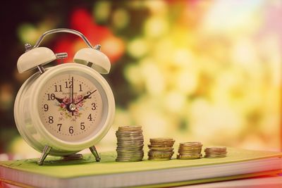 Close-up of clock and stacked coins on book