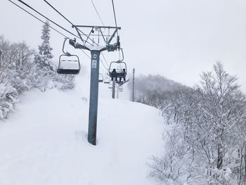 Ski lift by snow covered trees against sky