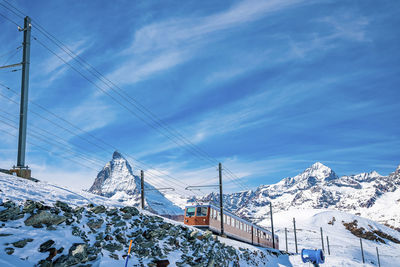 Red train passing through snowy matterhorn mountain against sky during winter
