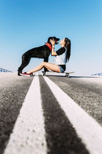 Woman with dog and skateboard against clear blue sky