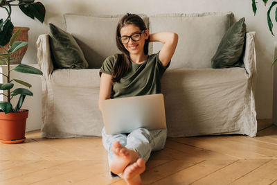 Young woman using laptop while sitting on sofa at home