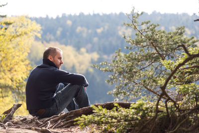 Man sitting on rock against sky