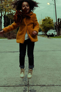 Portrait of happy girl in warm clothing jumping on road during sunset