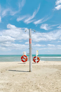 Front beach with shower pole and two red lifebuoys. blue sky with clouds.