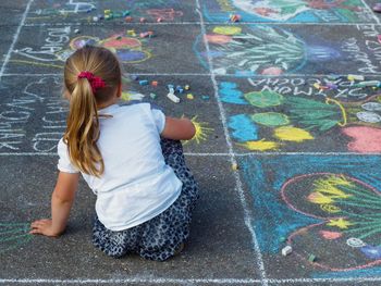 Rear view of girl sitting on chalk drawing at street