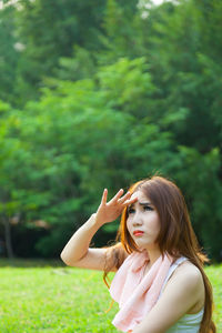 Woman shielding eyes while sitting on field