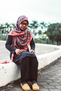 Thoughtful young woman sitting on dividing line at street