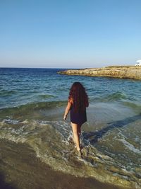 Rear view of woman walking on beach against clear sky