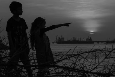 Silhouette girl pointing with friend at beach