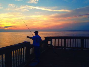 Man fishing on calm sea at sunset