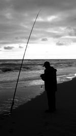 Rear view of silhouette man fishing on beach
