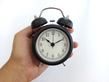 Cropped hand of person holding alarm clock against white background