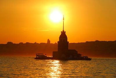 Silhouette of lighthouse in sea during sunset