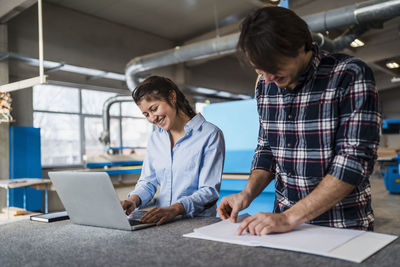 Smiling businesswoman using laptop while working with colleague at industry