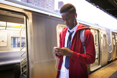 Student listening music while standing by train at railroad station