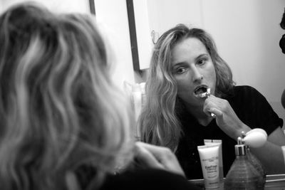 Young woman brushing teeth in front of mirror