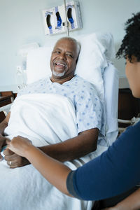 Happy father talking with daughter while leaning on bed in hospital ward