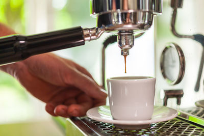 Close-up of person holding cup at espresso maker 