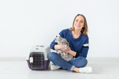 Portrait of smiling young woman sitting on floor against white background