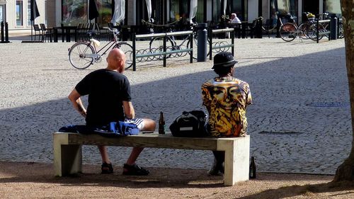 Rear view of men sitting on bench by cobbled street in city