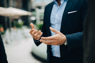 Midsection of mature businessman gesturing while standing amidst female colleagues in city