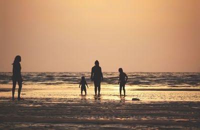 Silhouette people on beach against sky during sunset