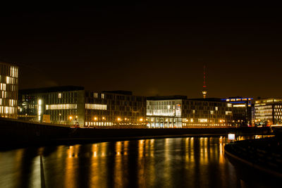 Illuminated city by river against sky at night