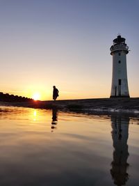 Lighthouse by sea against sky during sunset