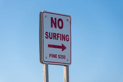 Low angle view of no surfing sign against clear blue sky