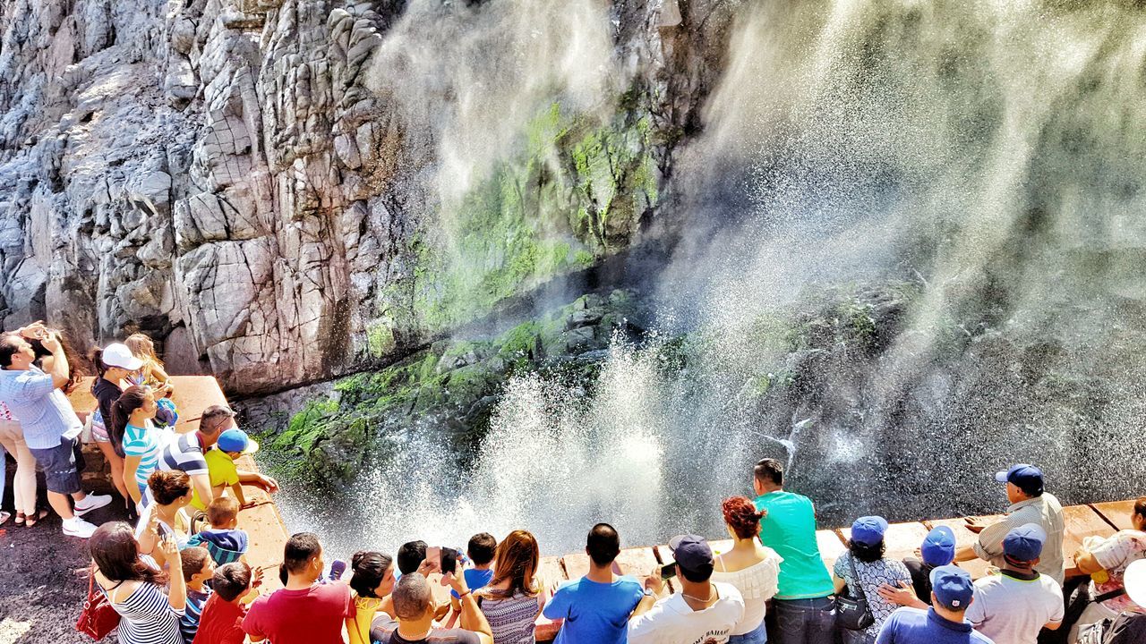 water, lifestyles, leisure activity, large group of people, men, motion, person, vacations, enjoyment, waterfall, standing, splashing, surf, tourist, rock - object, travel, tourism, flowing water, togetherness