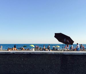 People at beach against clear blue sky