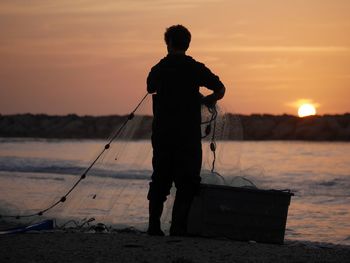 Rear view of silhouette man fishing on beach during sunset