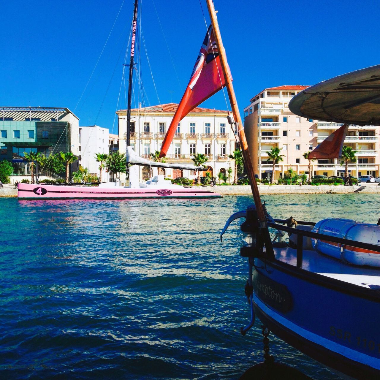 nautical vessel, water, boat, building exterior, moored, clear sky, transportation, mode of transport, blue, built structure, architecture, waterfront, canal, sunlight, incidental people, day, tree, travel, harbor, outdoors